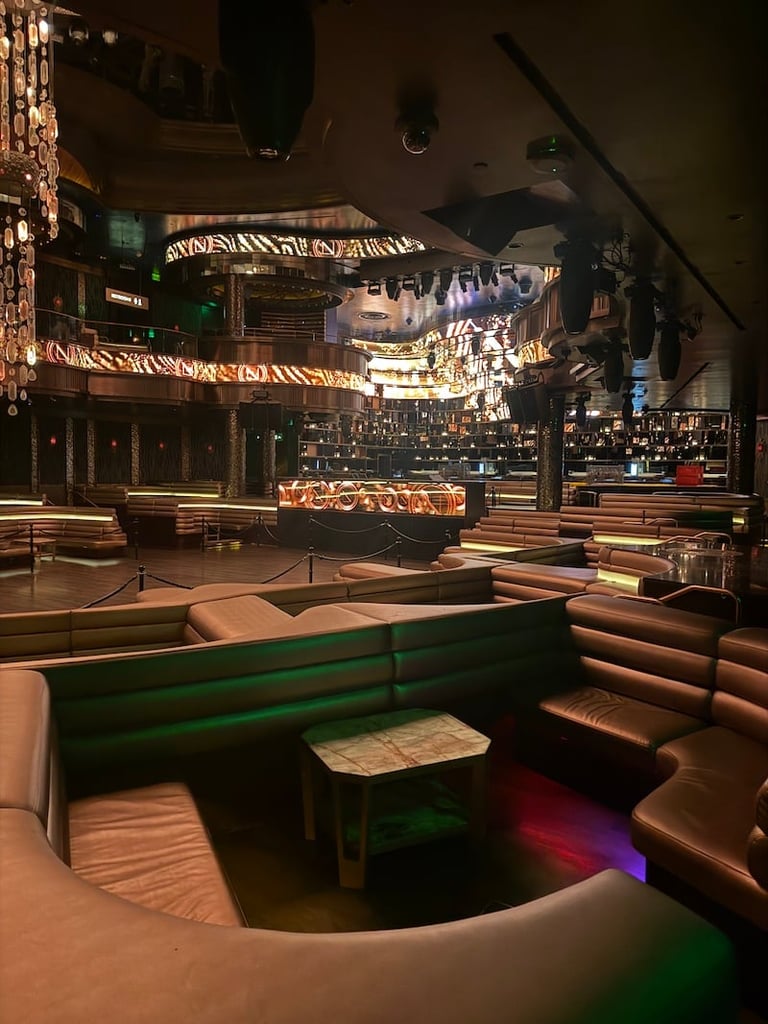 Modern nightclub interior with curved seating booths, illuminated bar counter, and city skyline backdrop on screens
