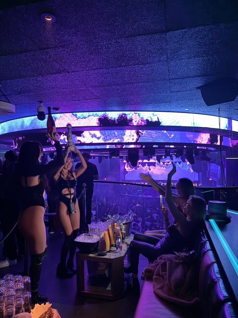 Interior of nightclub with purple and blue neon lighting, bar counter, and people socializing in a modern venue