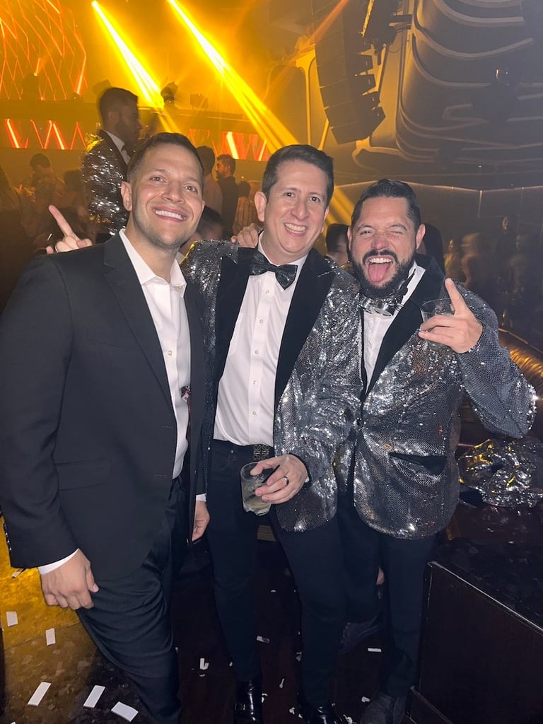 Three men in formal attire smiling at camera in front of gold neon lights at an event venue
