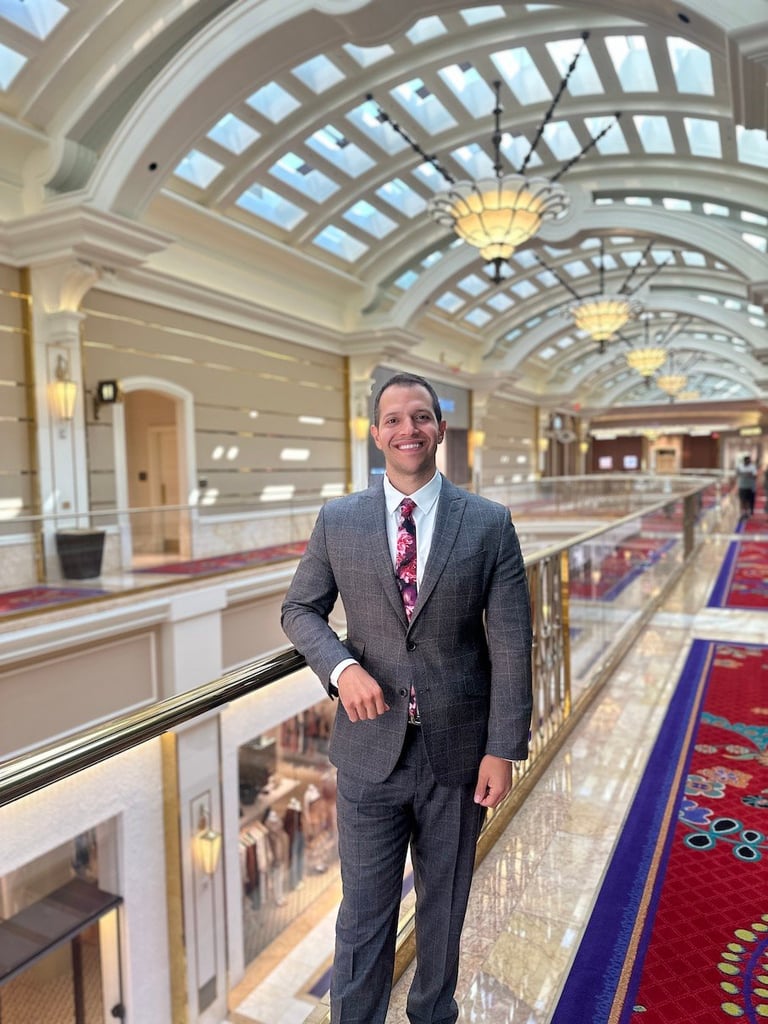 Man in gray suit standing on a balcony inside an elegant building with arched glass ceiling and skylights